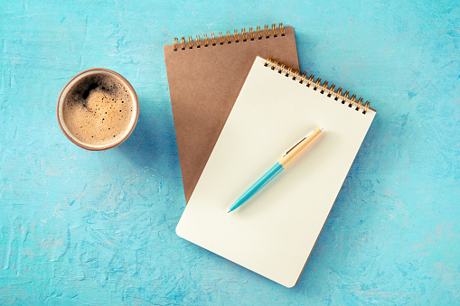 Notebook mockup with a pen and a cup of coffee, overhead flat lay shot on a blue background