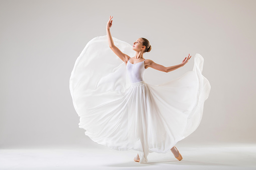 young ballerina in pointe shoes dances in long flying white skirt on a white background