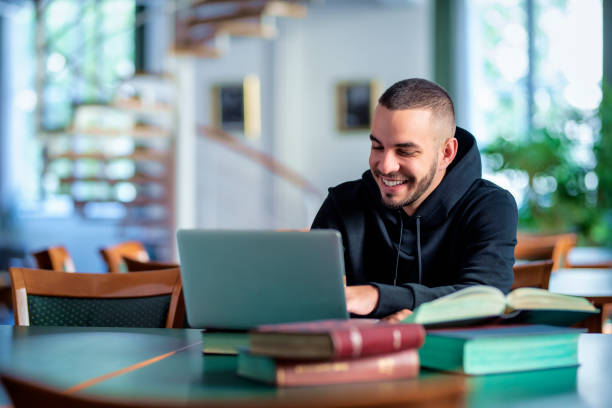 Male student using notebook and books and learning in the university library stock photo