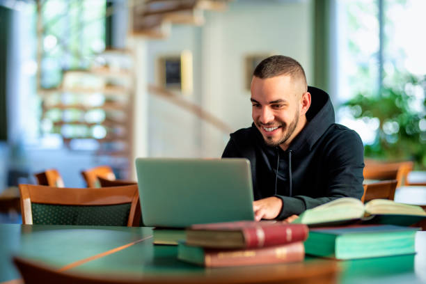 istock Male student using notebook and books and learning in the university library 1847538131