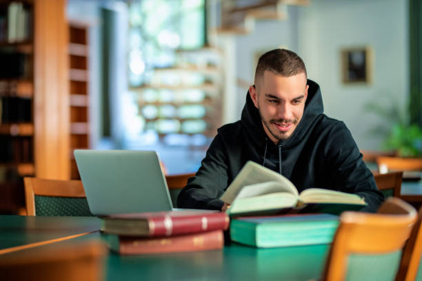 istock Male student using notebook and books and learning in the university library 1847538299