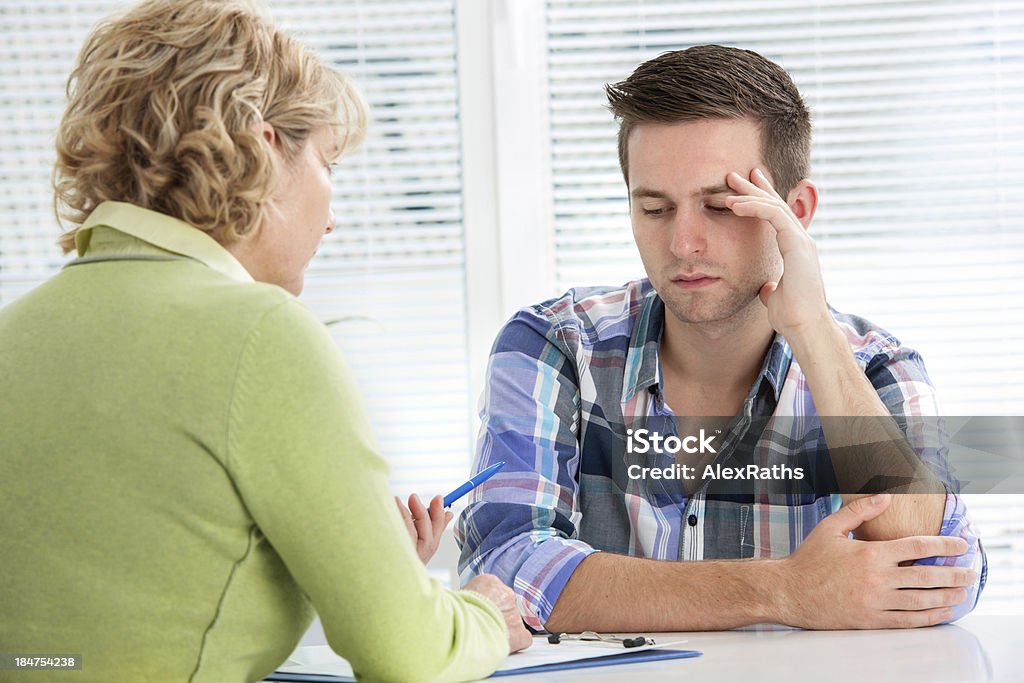 Un medico e un adulto seduto a un tavolo - Foto stock royalty-free di Adolescente