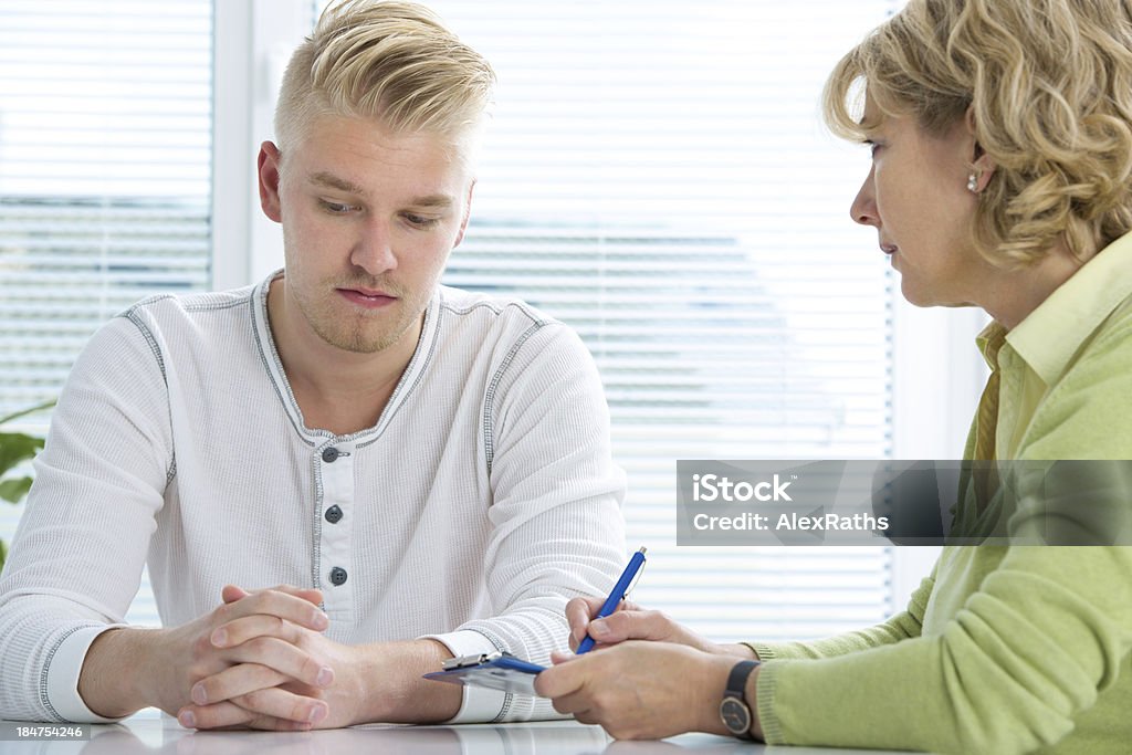 A doctor taking notes with a young male patient Young man visits doctors office suffering with depression Adolescence Stock Photo