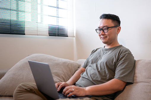 Asian Chinese male with glasses working on laptop on a comfortable sofa