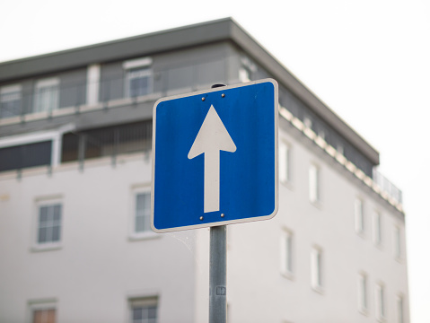 One-way street sign in Germany. The white arrow on the blue square is pointing ahead. The travel direction is straight on.