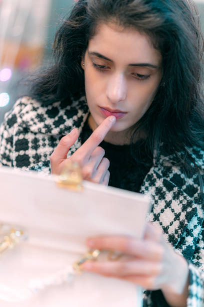 Woman applies lip color or balm after snacking in a restaurant. After snacking in a restaurant, a woman applies lip color or balm while looking into the mirror inside the flap of her purse. restaurant mirror stock pictures, royalty-free photos & images