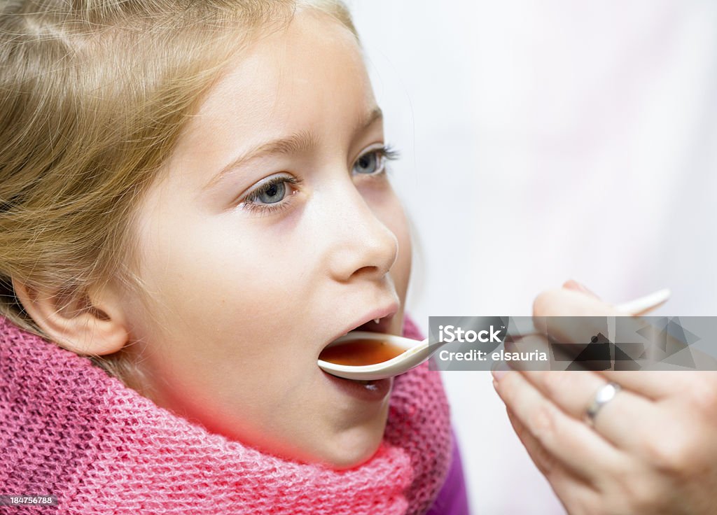 Girl taking medicine from a spoon. Girls Stock Photo