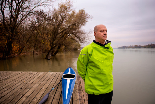 A middle-aged man standing on the jetty and ready to go kayaking. Active sporty man wearing dry suit and deep in thought.