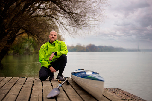 A middle-aged man standing on the jetty and ready to go kayaking. Active sporty man wearing dry suit and looking at camera.