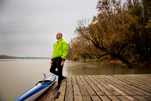 A middle-aged man standing on the jetty and ready to go kayaking. Active sporty man wearing dry suit and looking away.