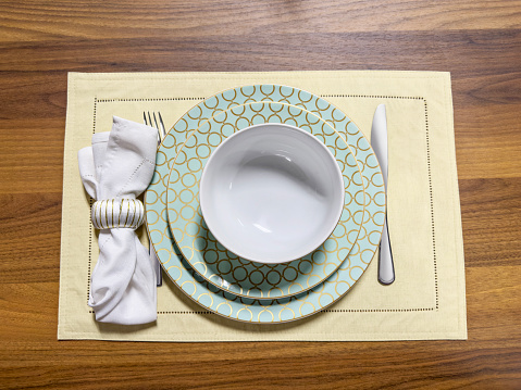 Looking down on a crockery set with napkin ring and napkin crockery on top of a wooden dining table