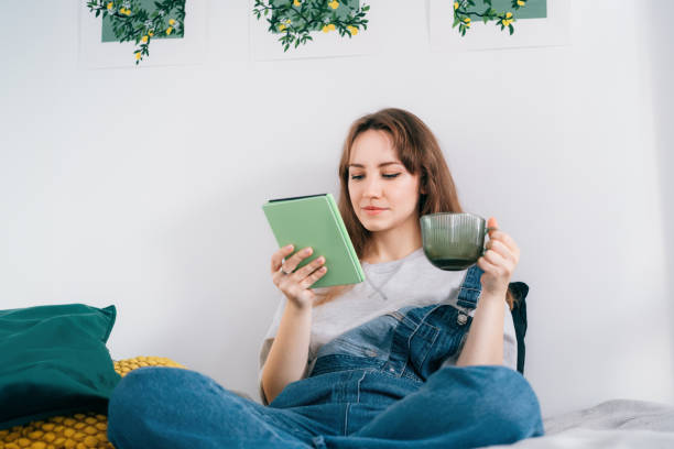 istock Young woman reading e-book on tablet reader in bed. Female relaxing with hot drink while reading an electronic book in cozy room. Mental health recovery, Personal growth. Hobby, Leisure time alone. 1847592265