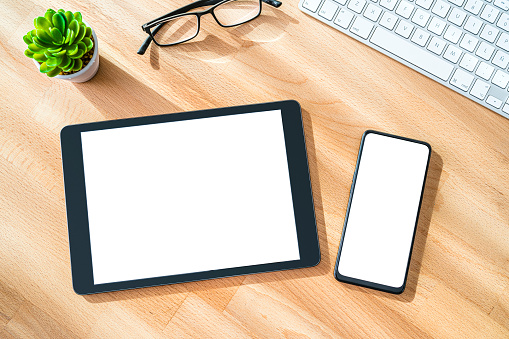 Overhead view of digital tablet and smartphone with blank mockup screen on wood workspace