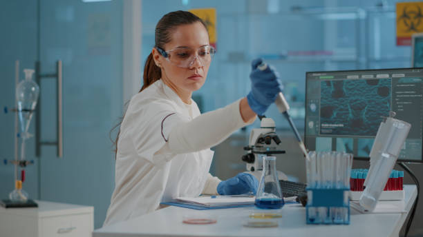 donna biologa che utilizza una micro pipetta con provetta e becher - test tube biologist laboratory beaker foto e immagini stock