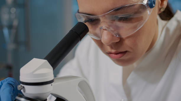 istock Woman looking through microscope lens to analyze dna sample 1847638185