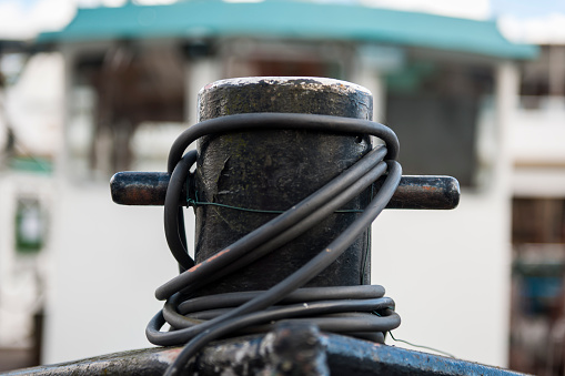 Close-up view of a black bollard of a cutter on the bow with folded power cables in front of the out-of-focus wheelhouse in the harbor of Leer in East Frisia.