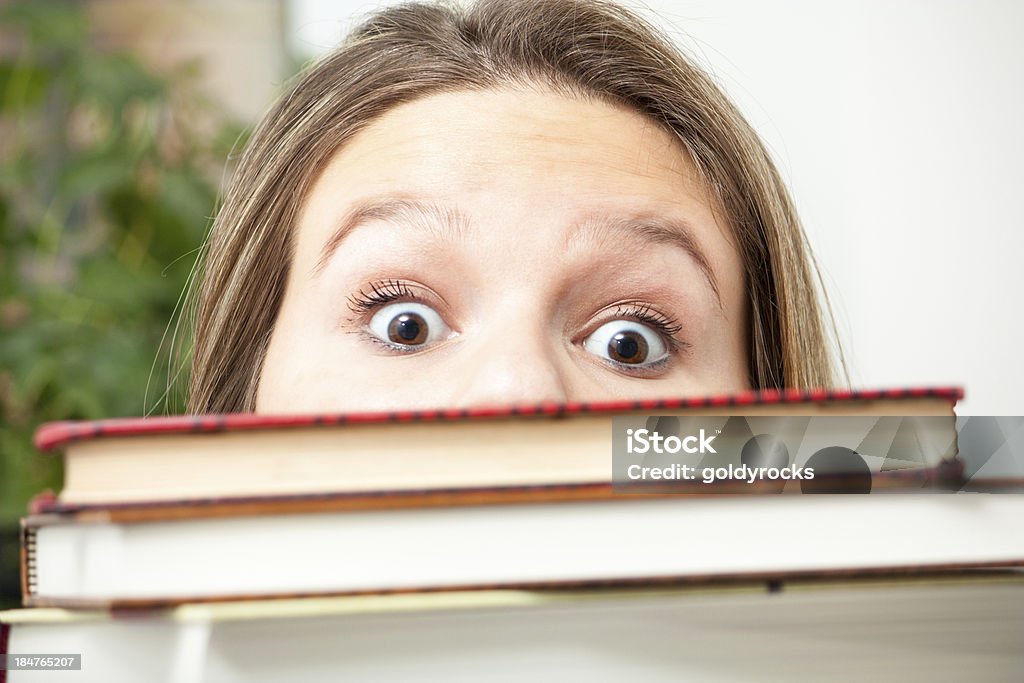 Study Shock horizontal A young college student peeks up over a big stack of books in panic over all the  homework she has to do. Adult Stock Photo