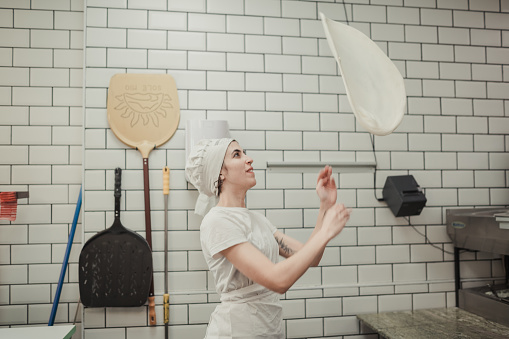 Portrait with copy space of a woman playing with a pizza dough in a restaurant kitchen