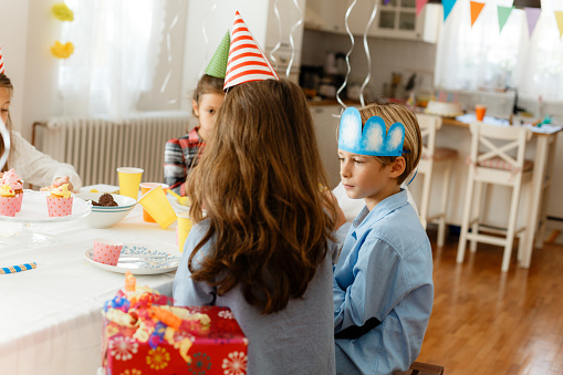 Group of children sitting at the table and eating cupcakes and sweets on a indoors Birthday party