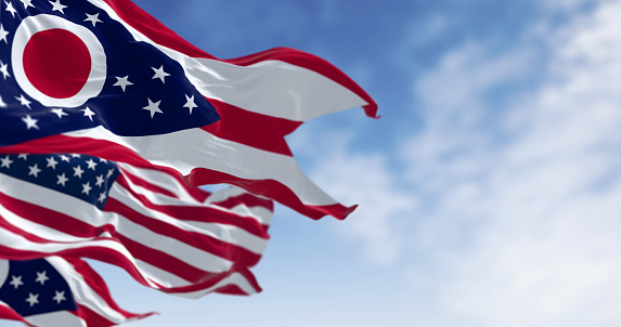 The Ohio state flag waving with the national flag of the United States of America on a clear day. 3D illustration render. Rippled textile. Selective focus