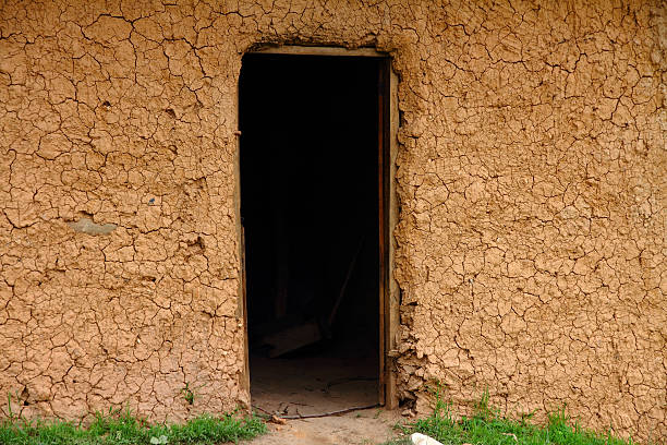 A cracked mud house exterior wall with a darkened doorway