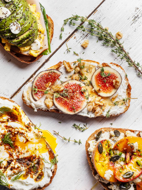 Sandwiches with fresh figs, cheese, thyme and honey on board. Fig bruschetta, bread and cream cheese and fruit on white background. Sandwiches with ricotta, fresh figs, walnuts and honey on white background. Bruschetta with figs, cheese, thyme. stock photo