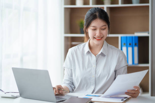 istock Attractive asian businesswoman sitting at work using laptop and examining many documents in office smiling. 1847811843