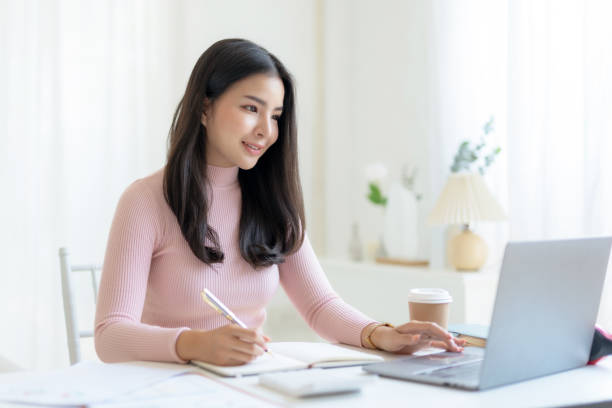 istock Young Asian woman sitting happily working and taking notes with laptop computer. 1847826239