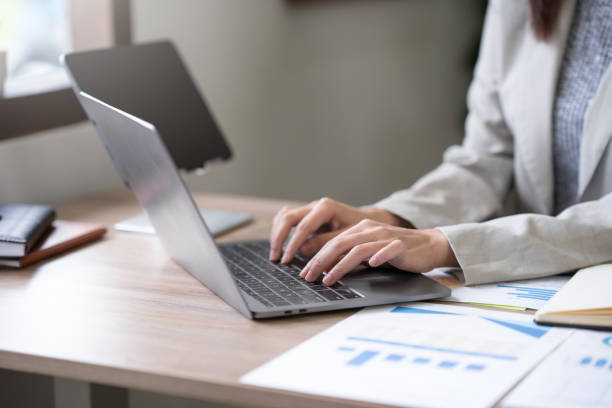 istock Close-up businesswomen using laptop computers to work attentively on a table with various documents such as charts and graphs of important financial data. 1847830651