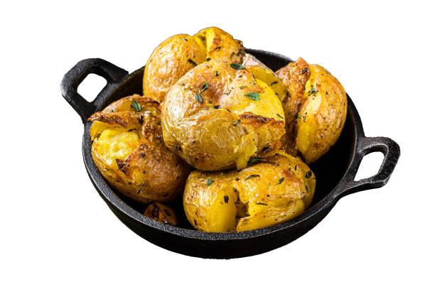 patatas trituradas y rotas al horno en aceite con hierbas.  aislado, fondo blanco. - smashed potatoes fotografías e imágenes de stock