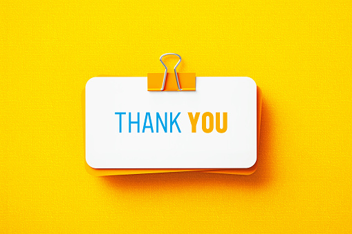 Thank you printed note held by an orange paper clip on yellow background. Horizontal composition with copy space.