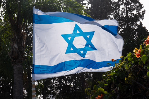 Independence day  (Yom Haatzmaut) in israel. Hanging official flag waving on wind with Star of David on it against trees.