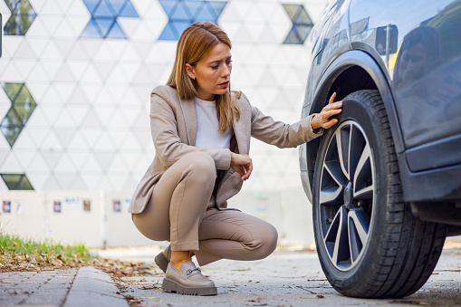 A snapshot of a mid-adult woman looking away in worry as she deals with a broken car on the roadside, reflecting the sudden interruptions and safety concerns in travel