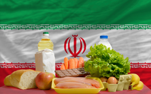 complete national flag of iran covers whole frame, waved, crunched and very natural looking. In front plan are fundamental food ingredients for consumers, symbolizing consumerism an human needs