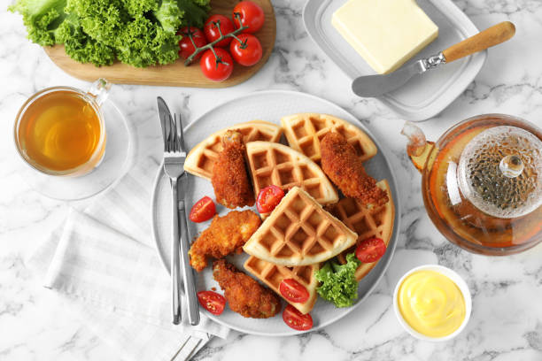 istock Tasty Belgian waffles served with fried chicken, tomatoes, lettuce and tea on white marble table, flat lay 1848021567