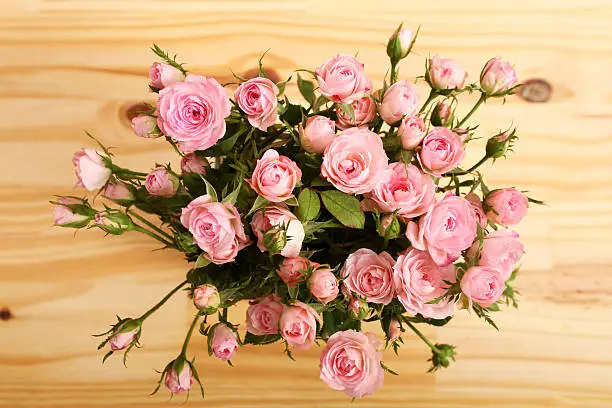 Bunch of small pink Roses in a glass vase over a wooden table.