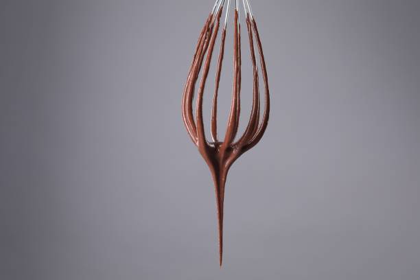 Chocolate cream flowing from whisk on grey background