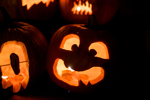 illuminated jack-o'-lanterns, each one telling a unique tale with spooky and cute faces carved into the pumpkins, lit up by the warm glow of candles for Halloween night.