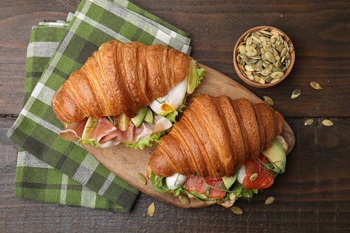 Delicious croissants with salmon, prosciutto and pumpkin seeds on wooden table, flat lay