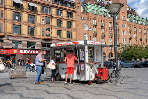 Copenhagen, Denmark - July 14, 2023: Customers at a traditional hot dog cart on the town hall square.