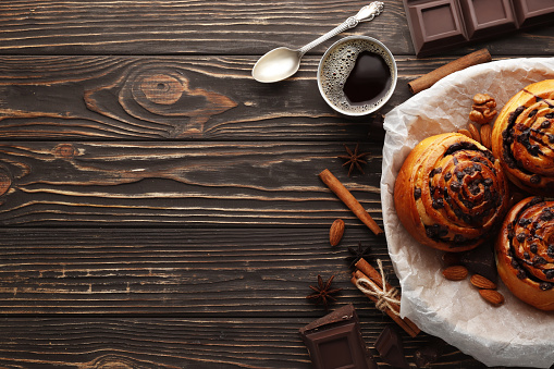Buns with cinnamon and chocolate on a brown wooden background. Cinnamon stick and black espresso coffee. Place for text. Top view.