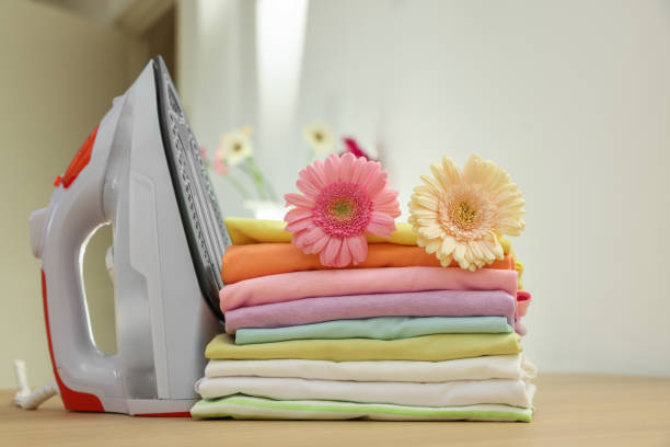 istock Stack of clean clothes, modern iron and flowers on wooden table 1848078491