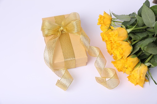 Gift box with golden bow and bouquet of beautiful roses on white background