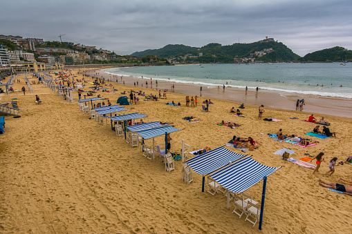 San Sebastian, Spain - August 13, 2023: Tourists bathing on La Concha beach on a cloudy summer day.