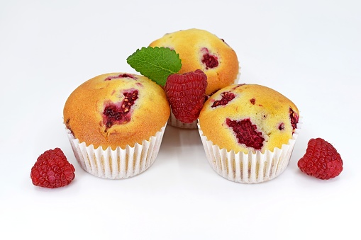 Muffins with raspberries on white background with fresh fruits, decorated with melissa leaf