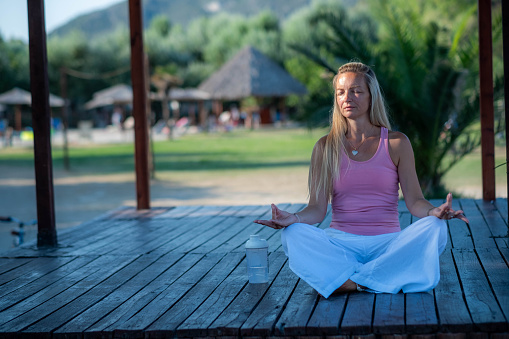young blonde woman sitting in yoga position outside with sunlights on face