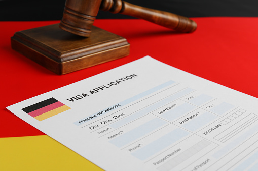 Immigration to Germany. Visa application form and wooden gavel on flag, closeup