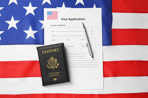 Immigration to USA. Visa application form, pen and passport on flag, top view