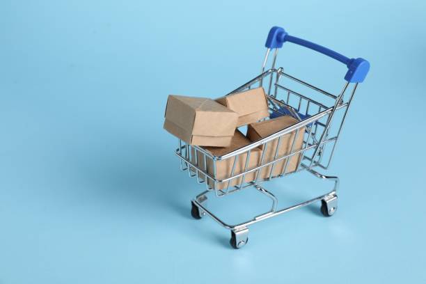 istock Small metal shopping cart with cardboard boxes on light blue background, space for text 1848111010