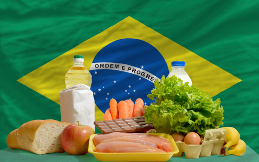 complete national flag of brazil covers whole frame, waved, crunched and very natural looking. In front plan are fundamental food ingredients for consumers, symbolizing consumerism an human needs